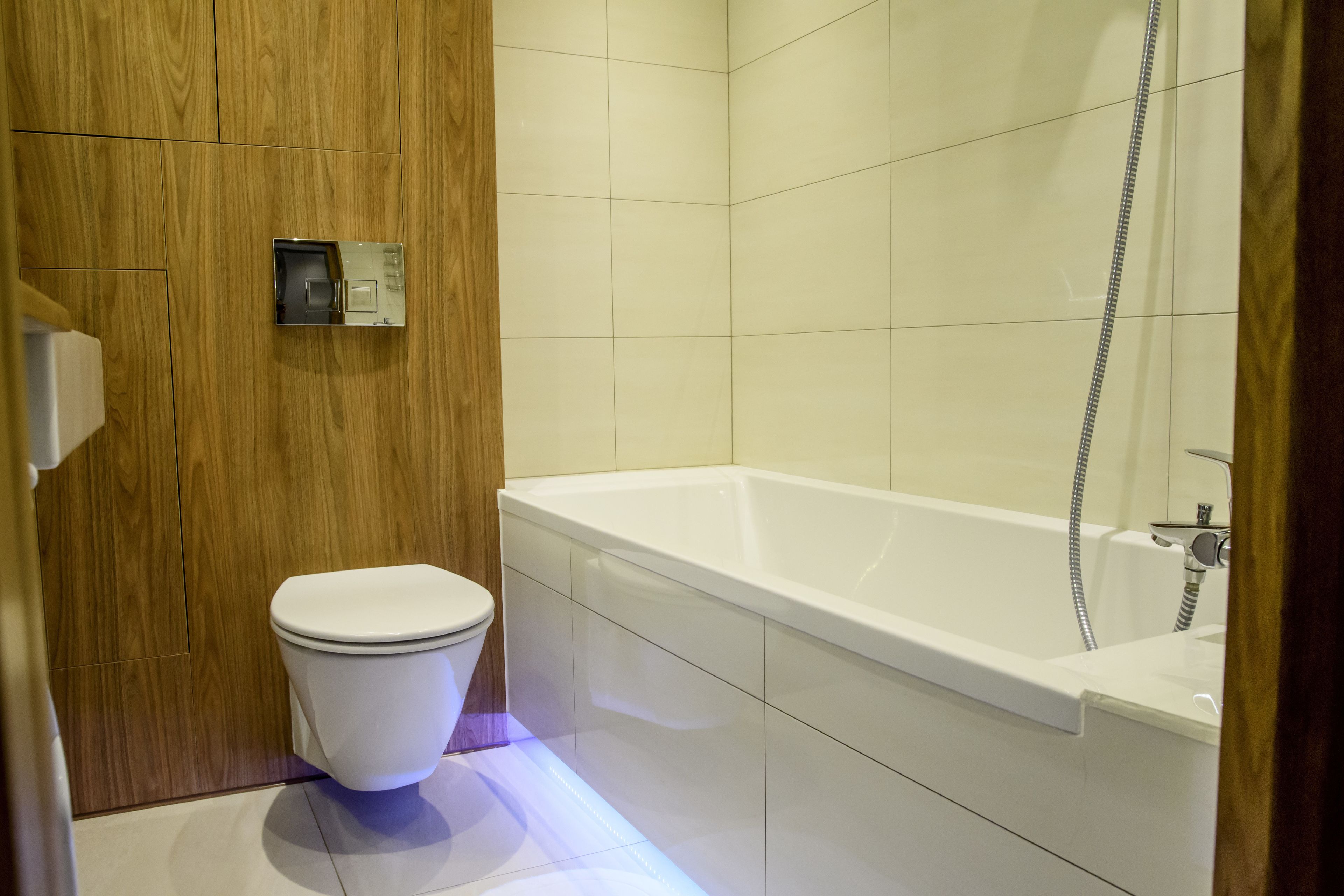 A modern bathroom with a wooden panel wall, a white toilet, and a white bathtub with a showerhead.