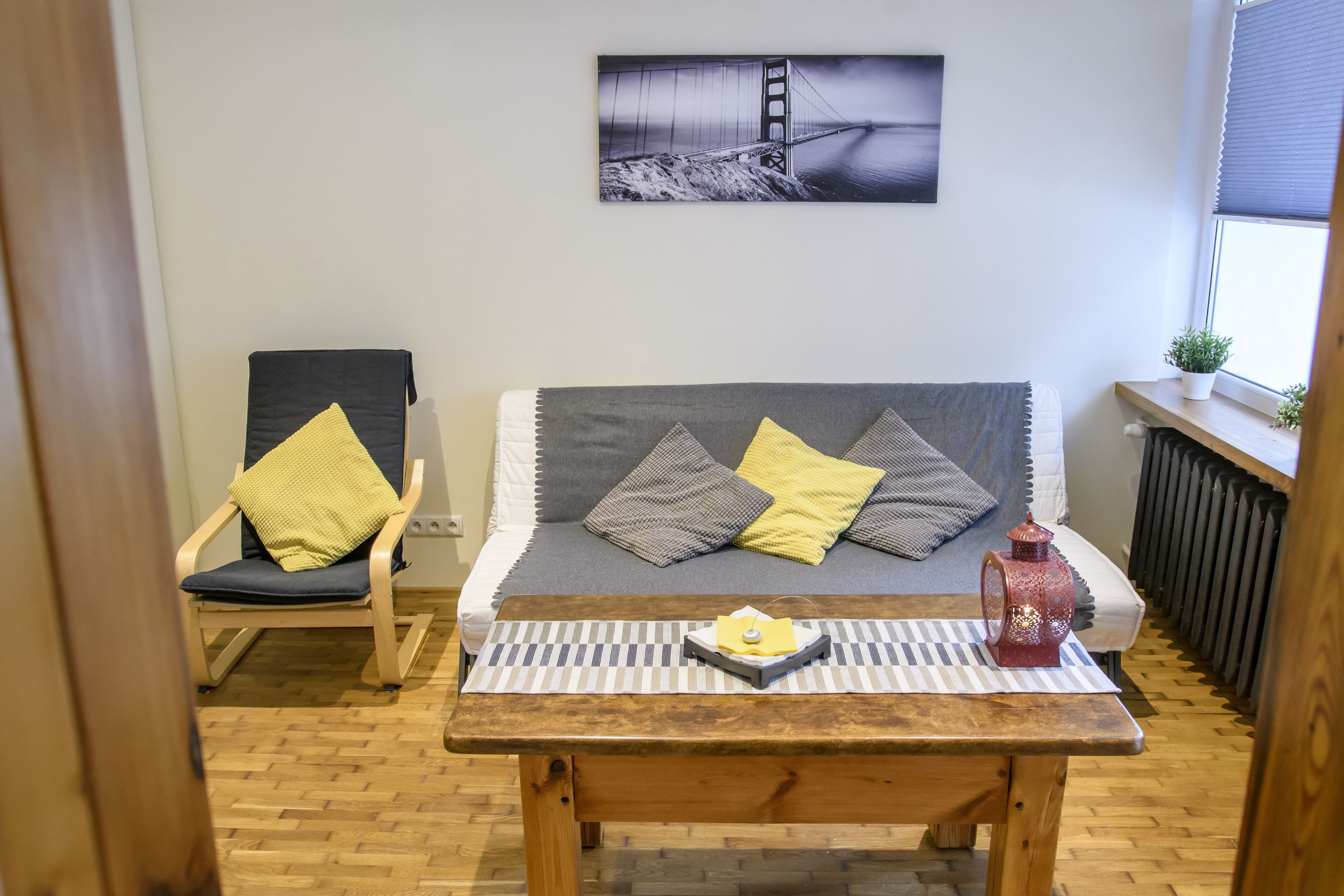 A cozy room with a sofa, a chair, and a table. There's a picture on the wall and a window with a plant.