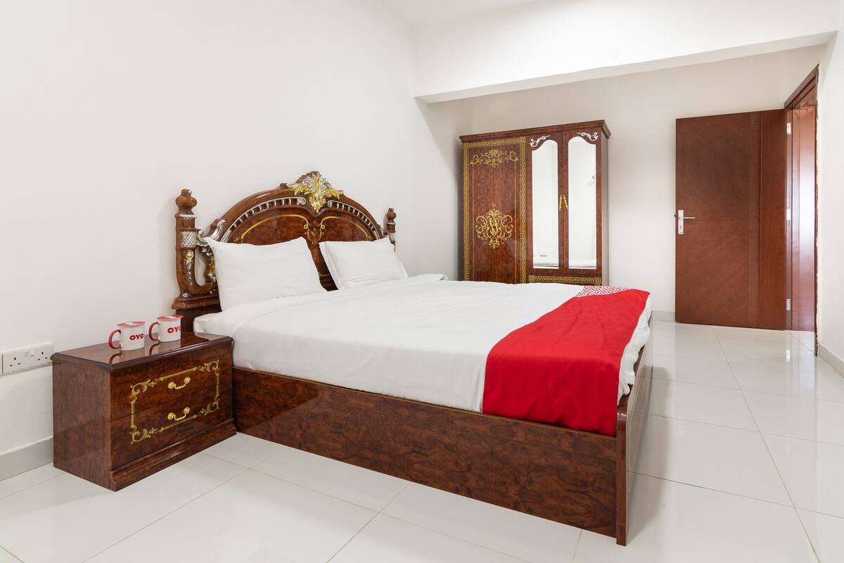 A neatly made bed with a wooden headboard, a nightstand with drawers, and a wardrobe with a mirror.