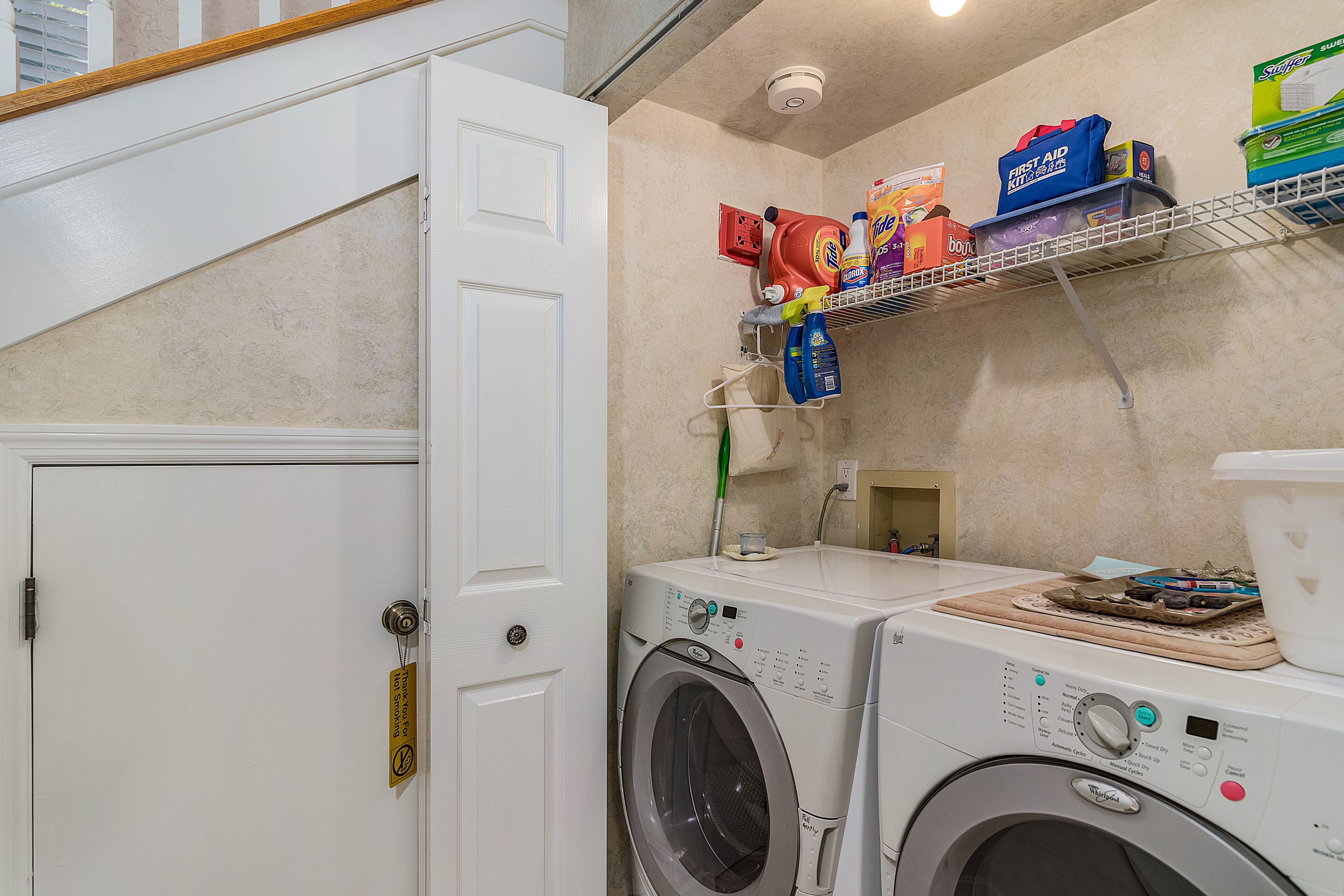 Un espace buanderie comprenant un lave-linge, un sèche-linge et une étagère avec des produits de nettoyage.