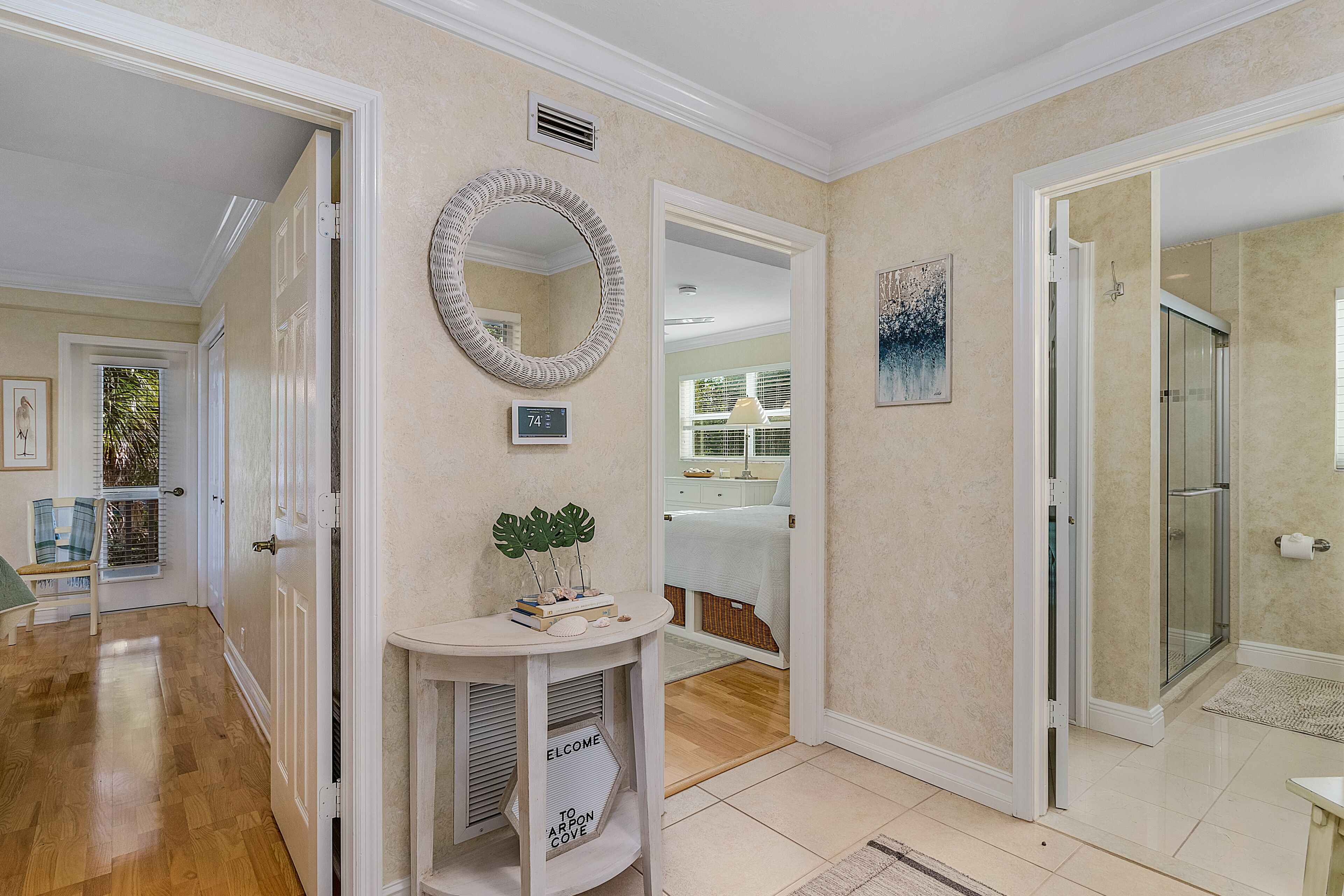 Un couloir avec une porte blanche, un miroir, un thermostat et un panneau d’accueil.