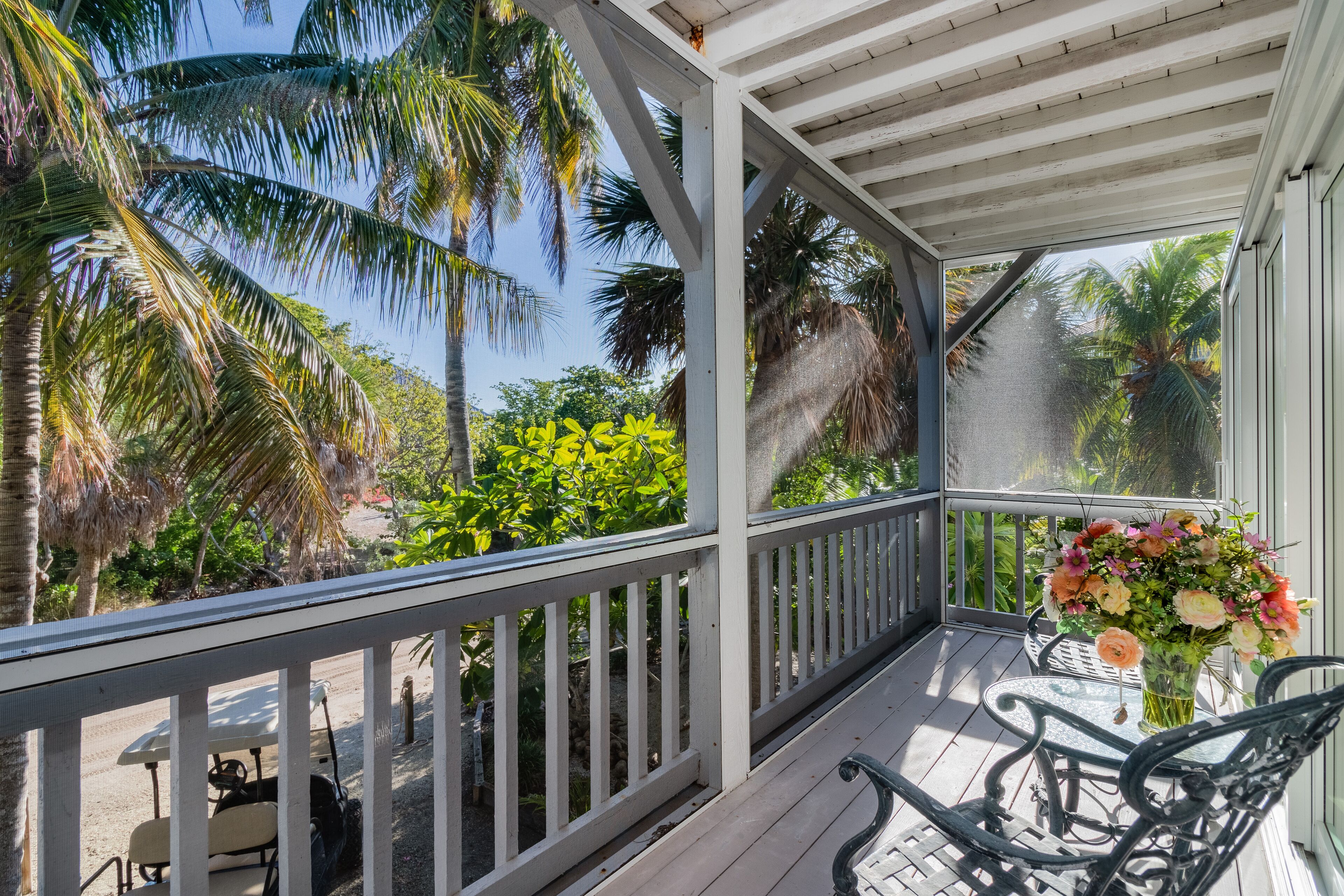A covered outdoor area with a wooden deck, metal chairs, and a table.