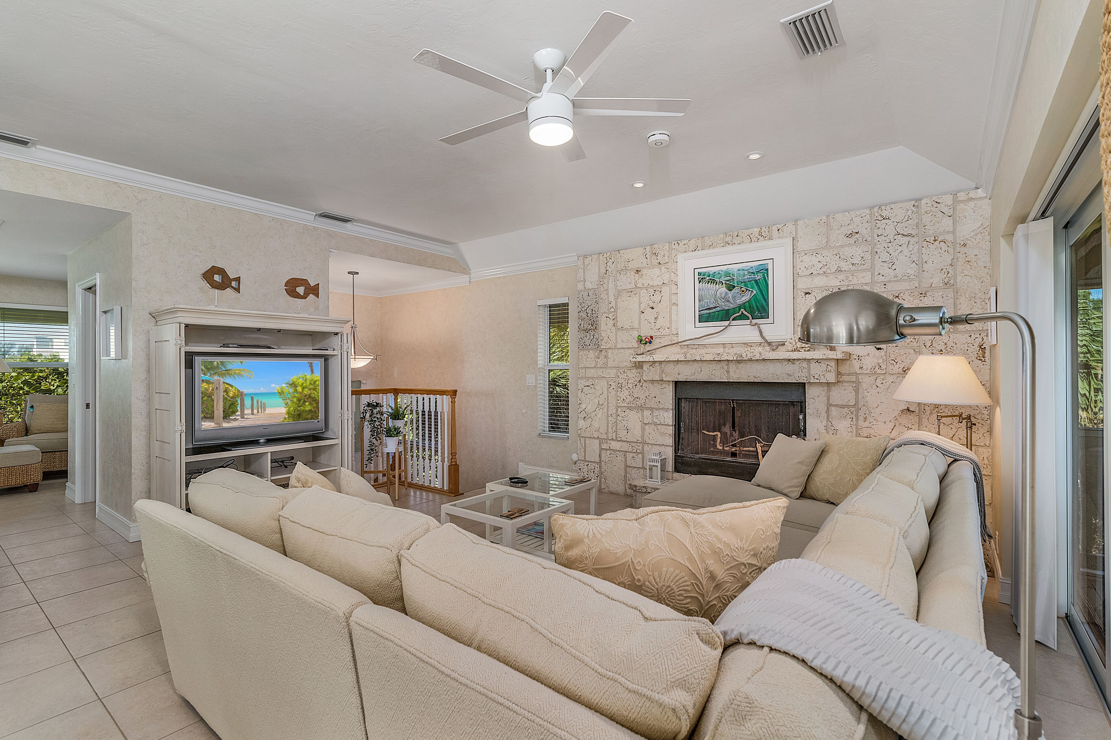 A living room with a beige sofa, a flat-screen TV, a fireplace, and a ceiling fan.