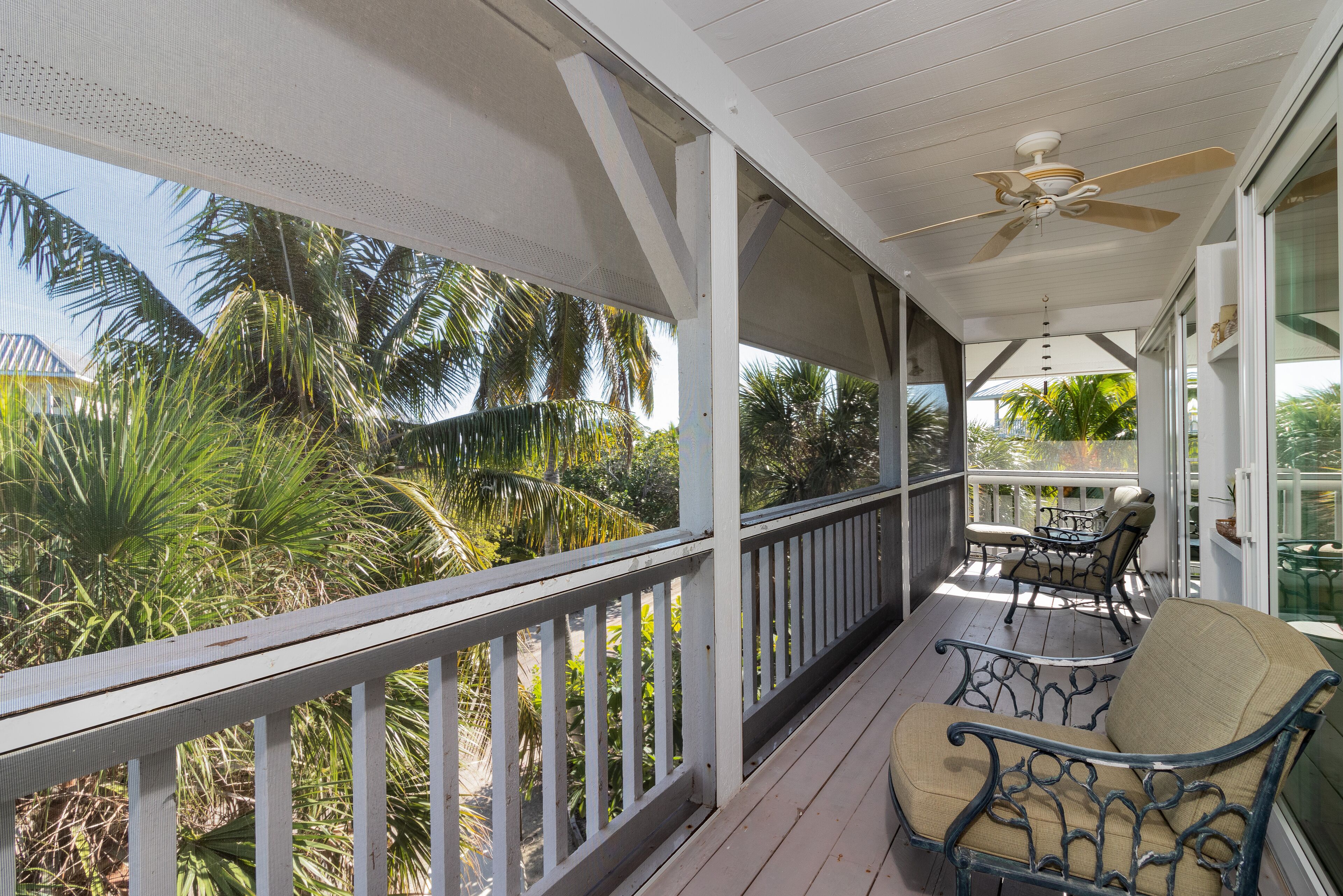 A covered porch with a ceiling fan, a table and chairs, and a view of palm trees.