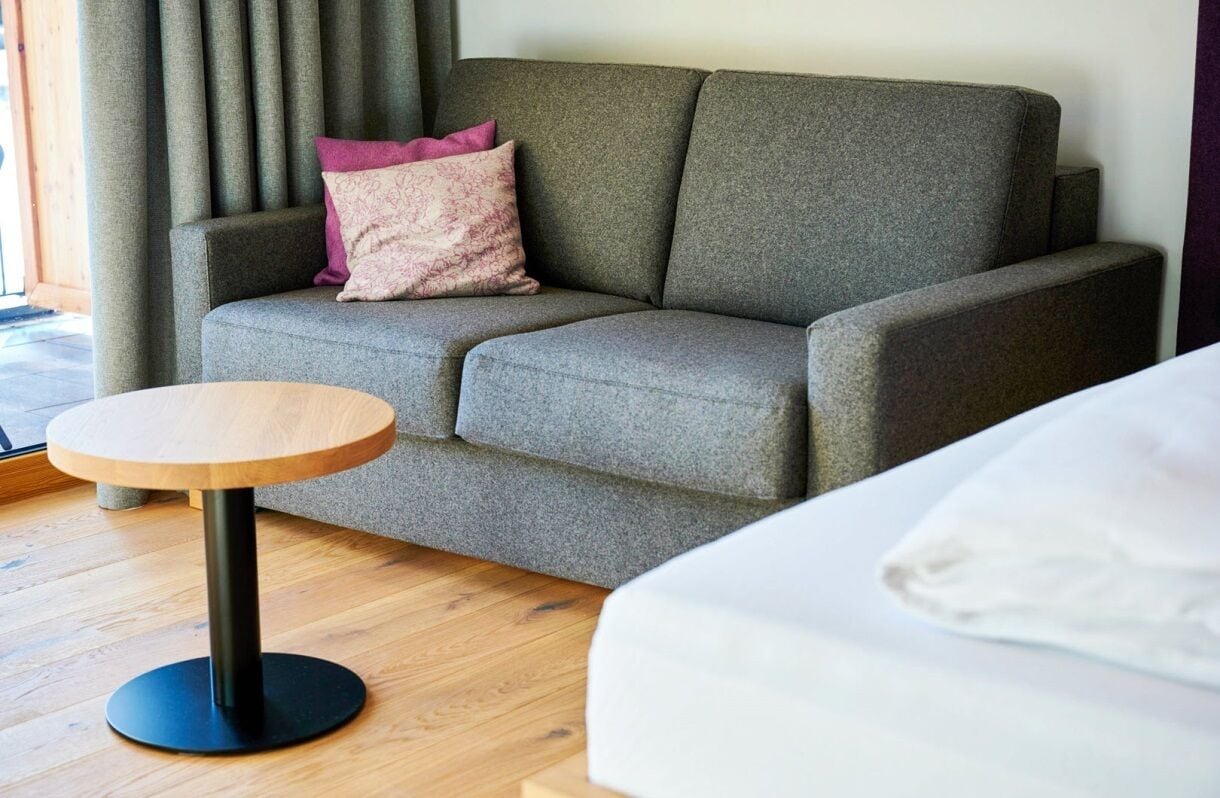 A modern room with a grey sofa, a round wooden table, and a white bed.