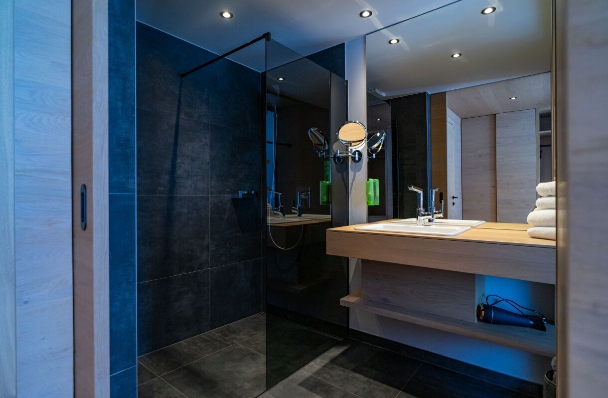 A modern bathroom with a glass shower enclosure, a wooden vanity with a mirror, and a towel rack.