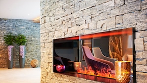 Ein modernes Interieur mit einer Steinwand, einem Kamin mit Glastür und einer Sitzecke mit Sofa und Sesseln.