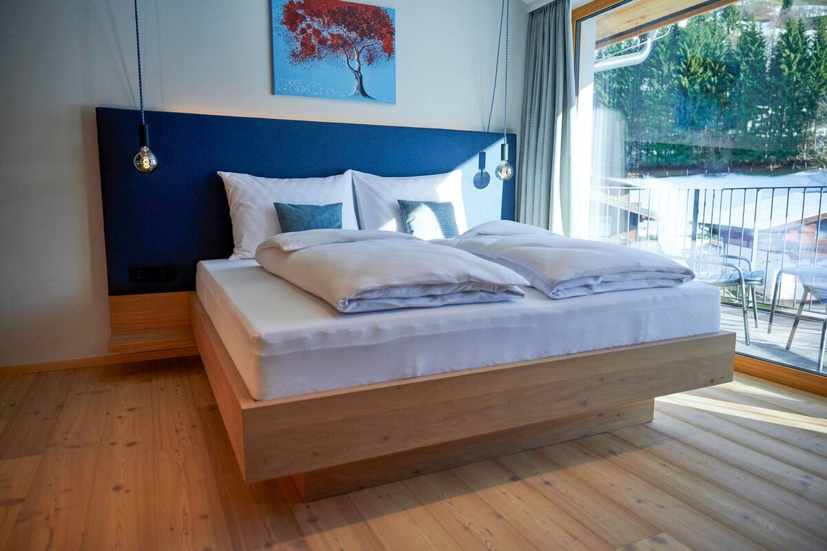 Ein modernes Schlafzimmer mit einem hölzernen Bett, einer blauen Kopfteil und Blick ins Freie.