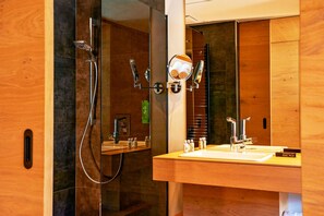 Un baño moderno con ducha cubierta por vidrio, tocador de madera con espejo y lavamanos.