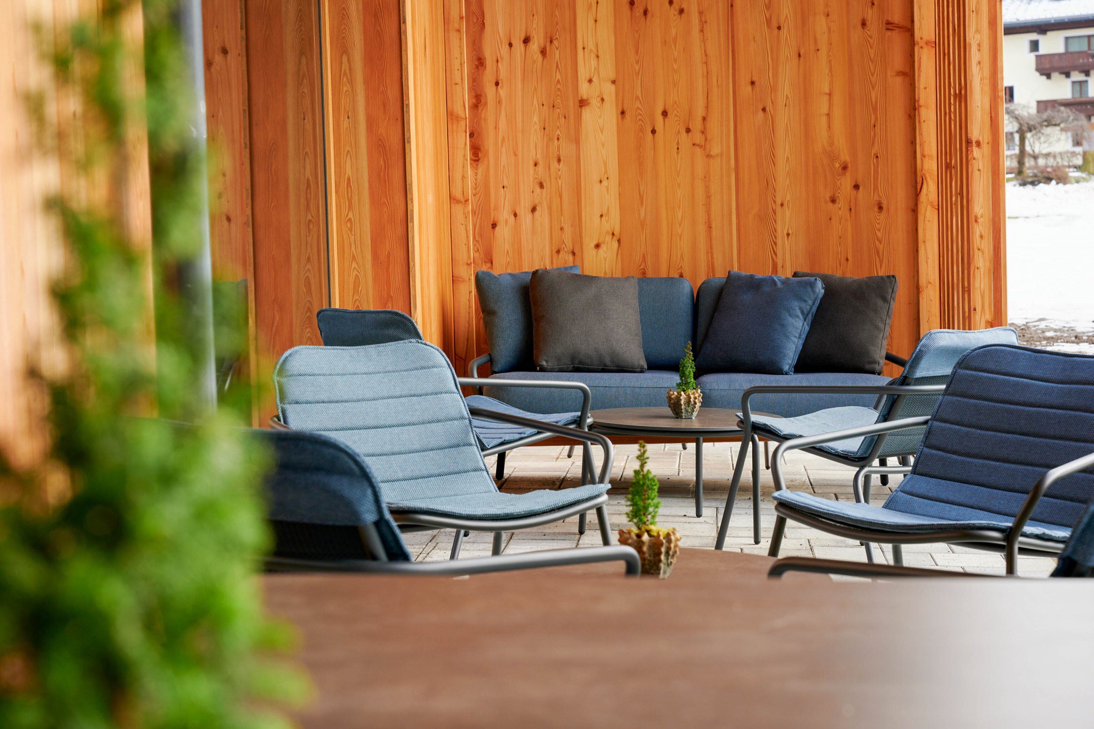 A wooden wall, a sofa with cushions, and two chairs with a small table in between.