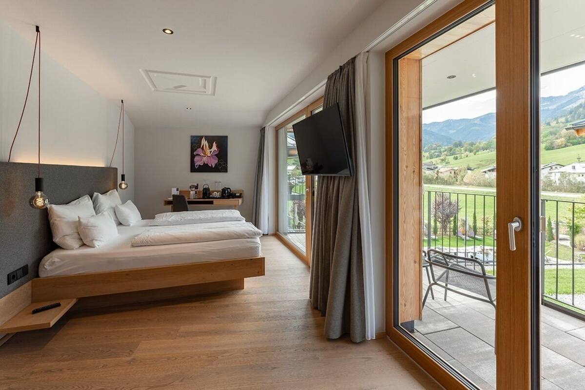 Ein Schlafzimmer mit Bett, Fernseher, einem Gemälde und einem Balkon mit Blick auf die Landschaft.