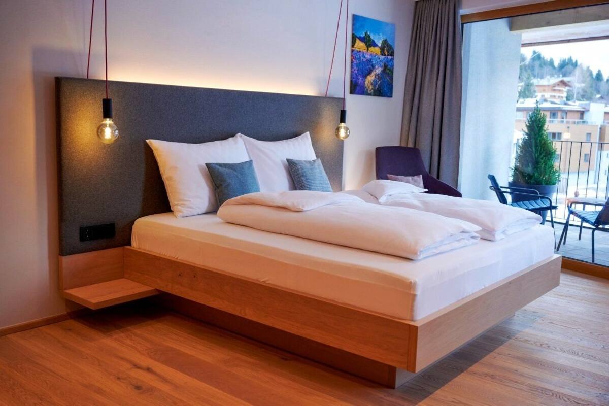 Ein modernes Schlafzimmer mit einem Holzbettgestell, einer Kopfteilbeleuchtung und einem Balkon mit Blick auf die Umgebung.