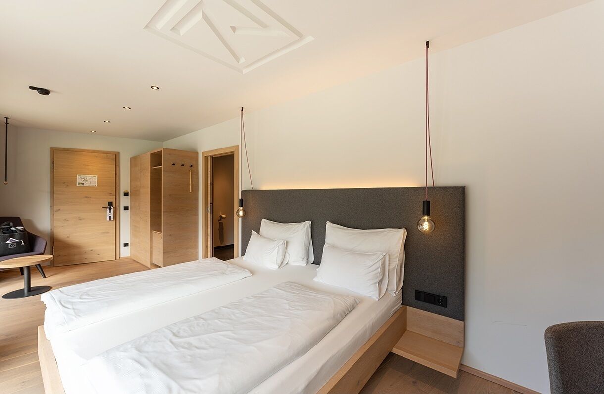 A modern hotel room with a large bed, a desk, and a wardrobe.