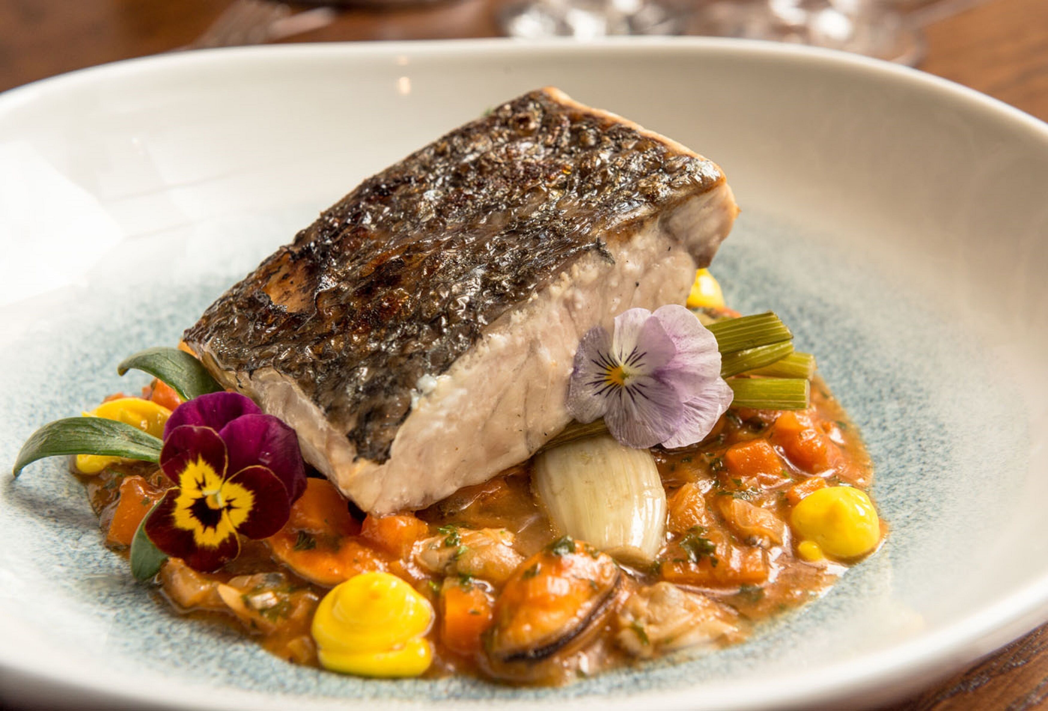A plate of food with a piece of fish, vegetables, and a flower garnish.