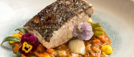 A plate of food with a piece of fish, vegetables, and a flower garnish.