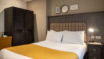 A neatly made bed with a plaid headboard, a bedside table with a lamp, and a wardrobe.