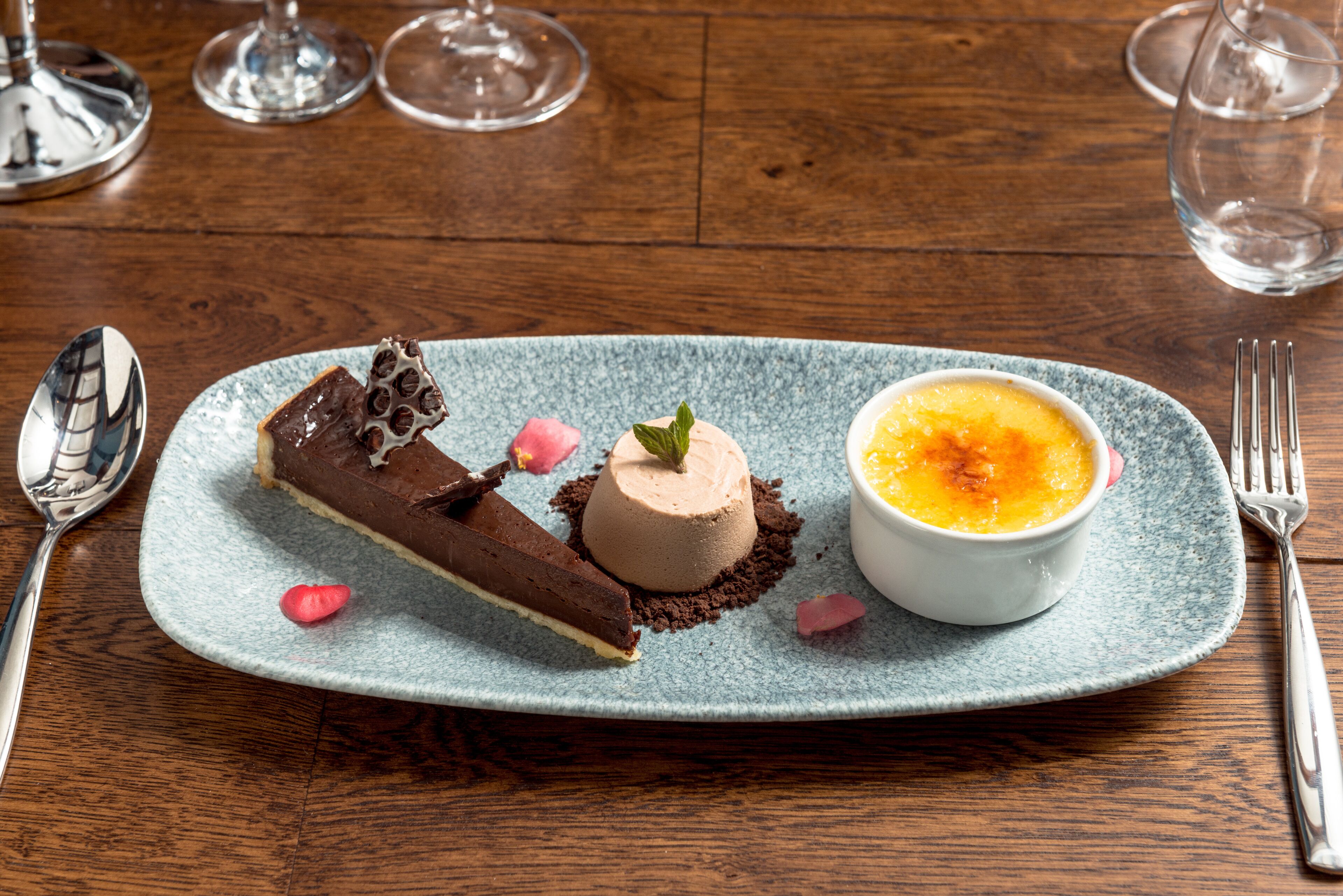 A dessert plate with chocolate mousse and a caramel flan on a blue ceramic plate.