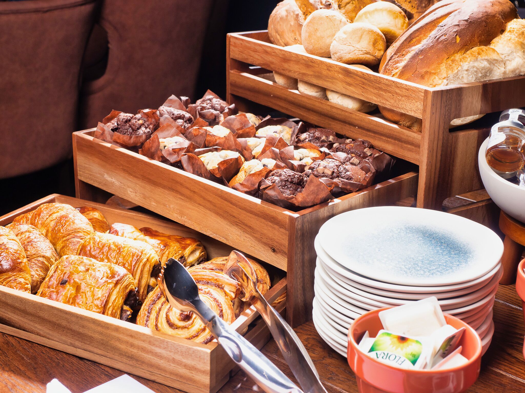 Diversas opciones de panadería y repostería en bandejas de madera, incluyendo pasteles y panes, con platos y una tetera a la vista.