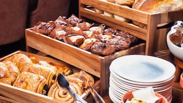 A variety of baked goods in wooden trays, including pastries and bread, with plates and a teapot visible.