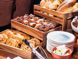 A variety of baked goods in wooden trays, including pastries and bread, with plates and a teapot visible. - The Feathers Hotel (Ludlow)