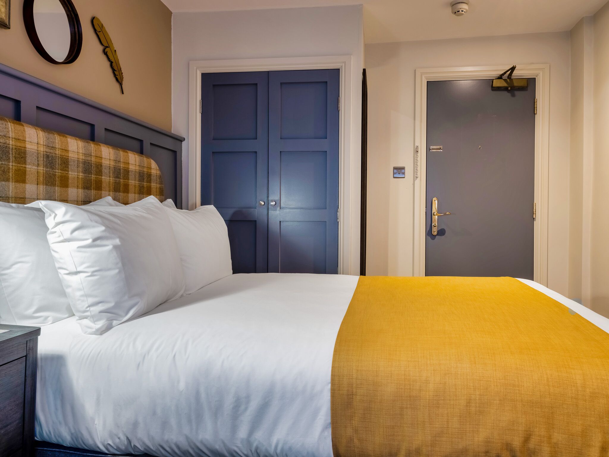 A hotel room with a bed, a headboard, a door, and a wall-mounted light fixture.