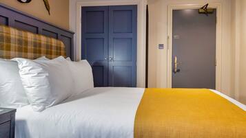 A hotel room with a bed, a headboard, a door, and a wall-mounted light fixture.