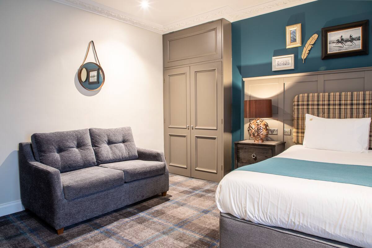 A bedroom with a grey sofa, a bed with a plaid headboard, and a wardrobe.