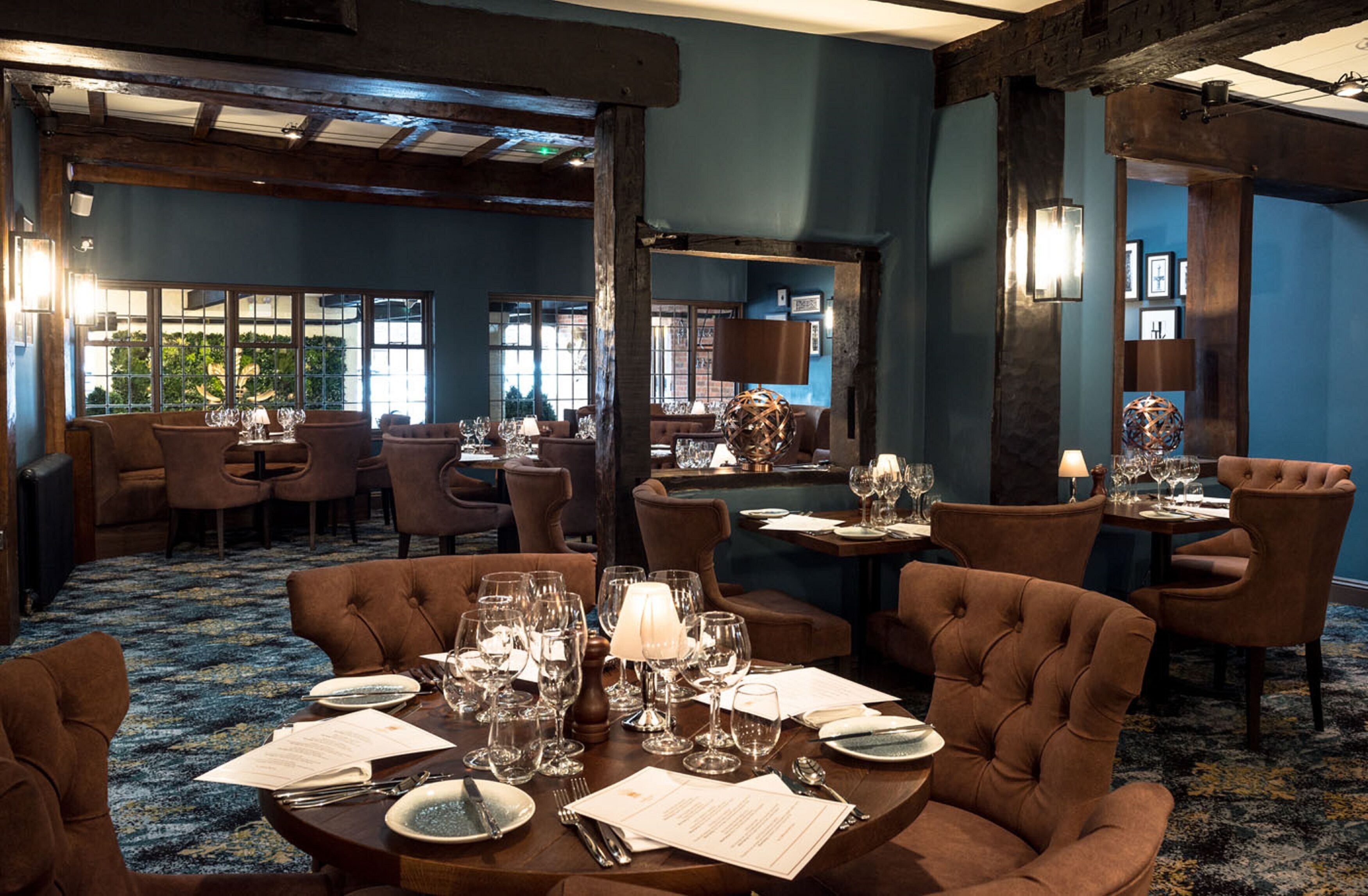 A restaurant with multiple dining tables set with wine glasses and plates, surrounded by upholstered chairs.