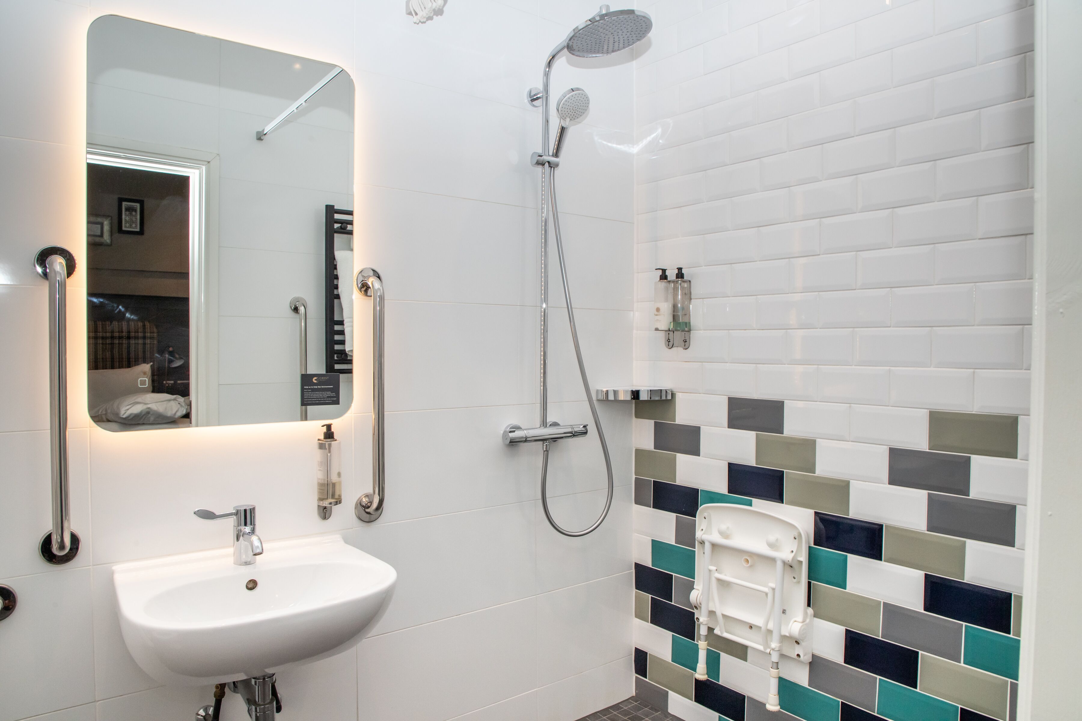 A modern bathroom with a white sink, a handheld showerhead, and a tiled wall with a geometric pattern.