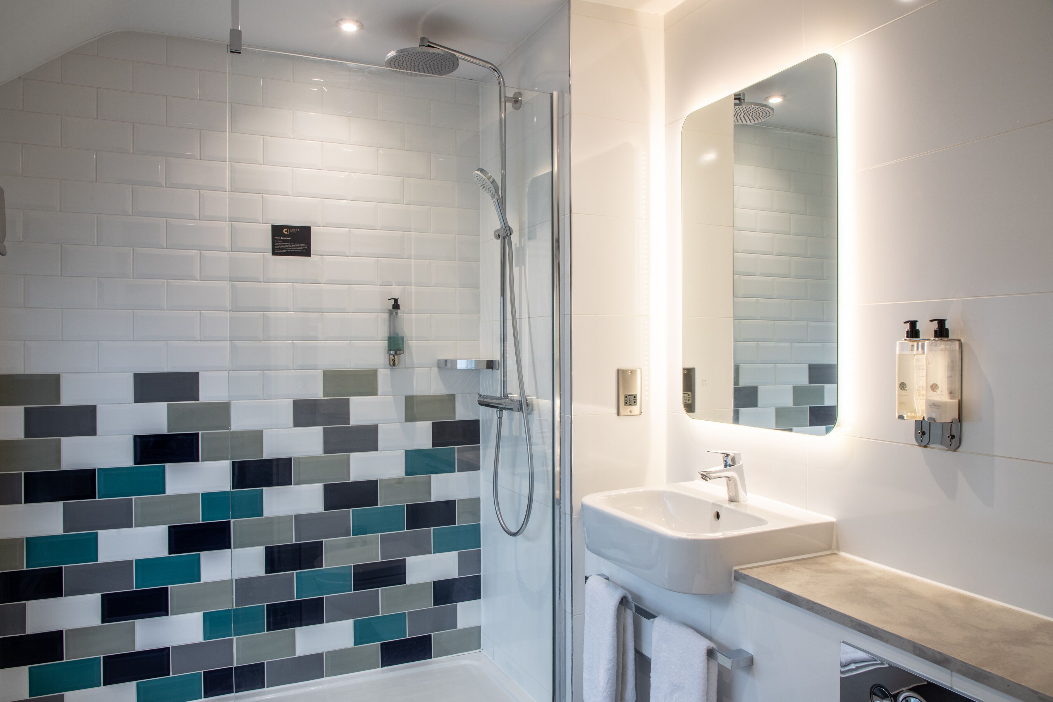 A modern bathroom with a glass-enclosed shower, a white sink, and a tiled backsplash.