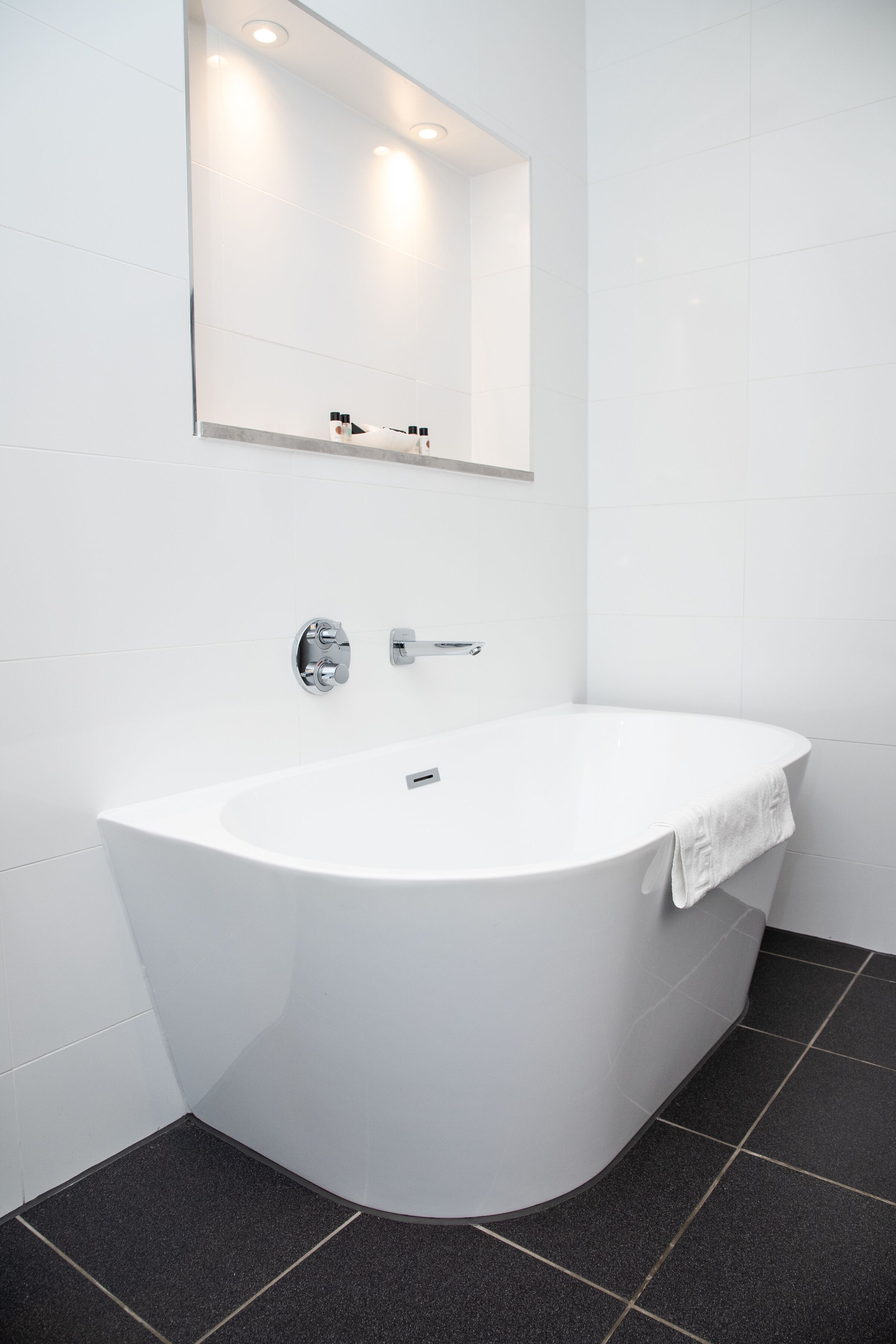 A modern bathroom with a freestanding bathtub, a wall-mounted mirror, and a towel hanging on the side.