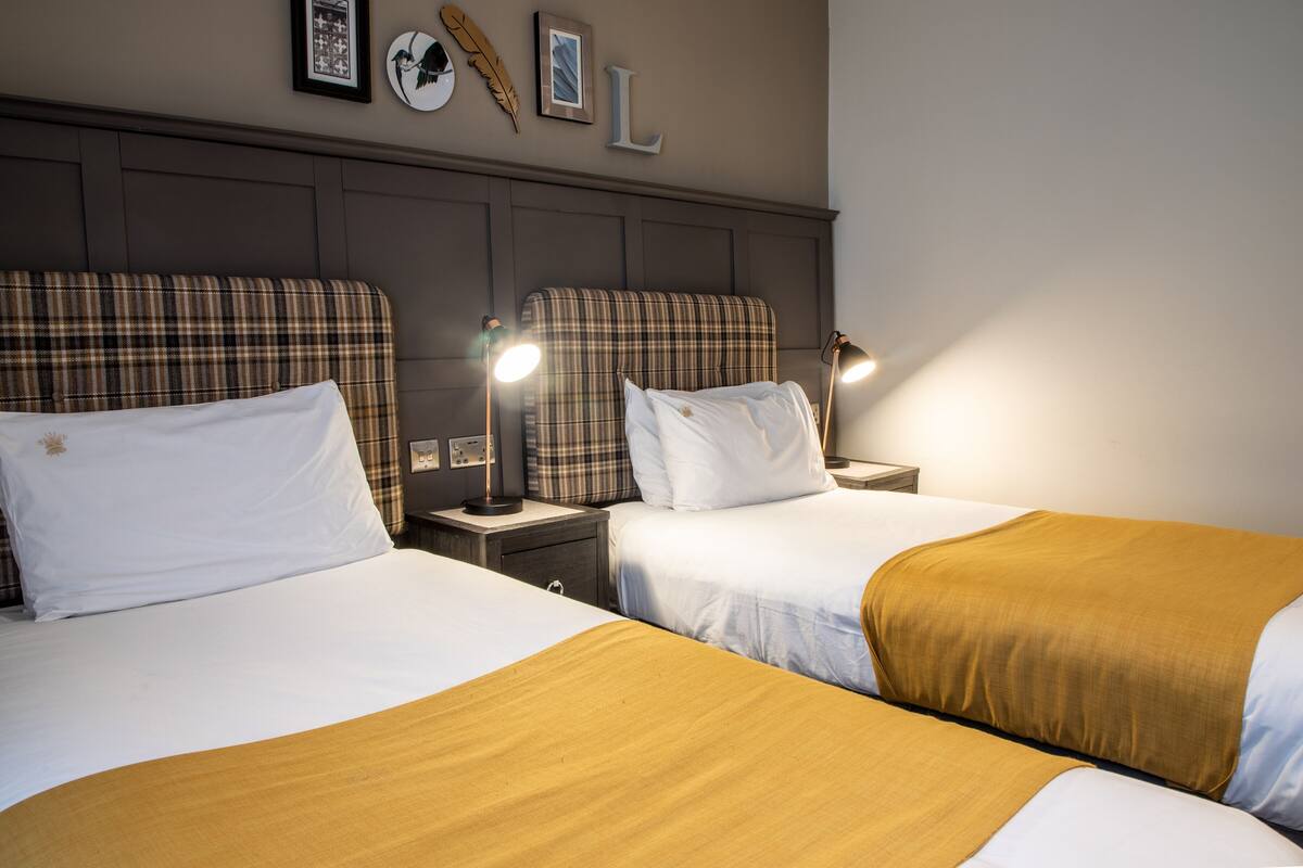 Two beds with plaid headboards, white bedding, and bedside lamps.