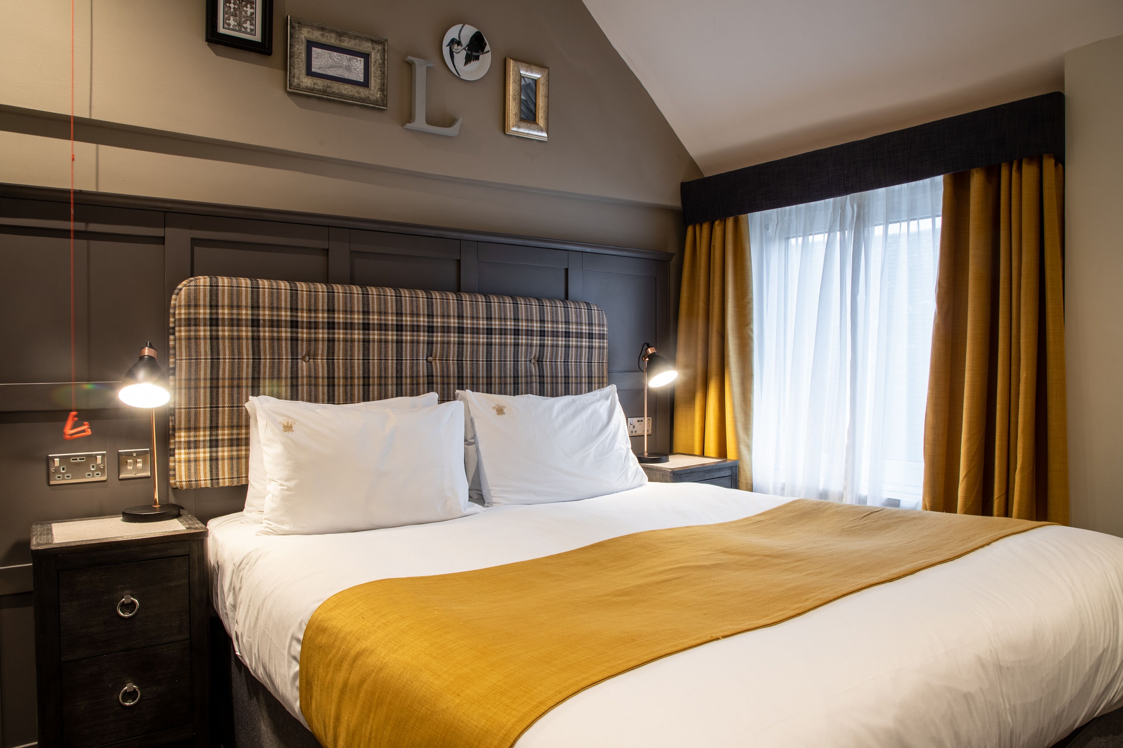 Une chambre d’hôtel avec un grand lit, une table de chevet avec une lampe, une tête de lit et une fenêtre avec des rideaux.