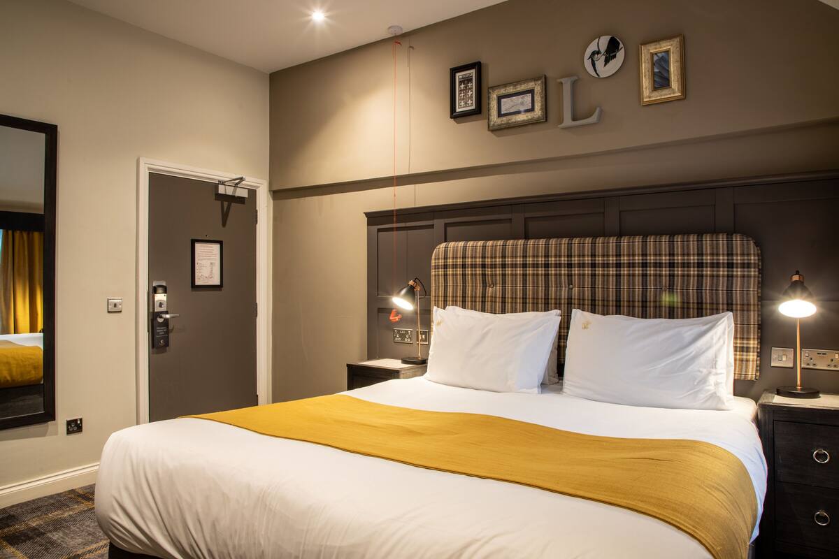 A hotel room with a large bed, a headboard, two bedside tables, a nightstand, a lamp, a mirror, and a door.