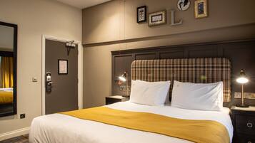 A hotel room with a large bed, a headboard, two bedside tables, a nightstand, a lamp, a mirror, and a door.