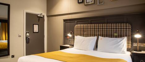 A hotel room with a large bed, a headboard, two bedside tables, a nightstand, a lamp, a mirror, and a door.