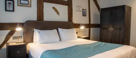 A bedroom with a large bed, wooden beams on the ceiling, two bedside tables with lamps, and a wardrobe.