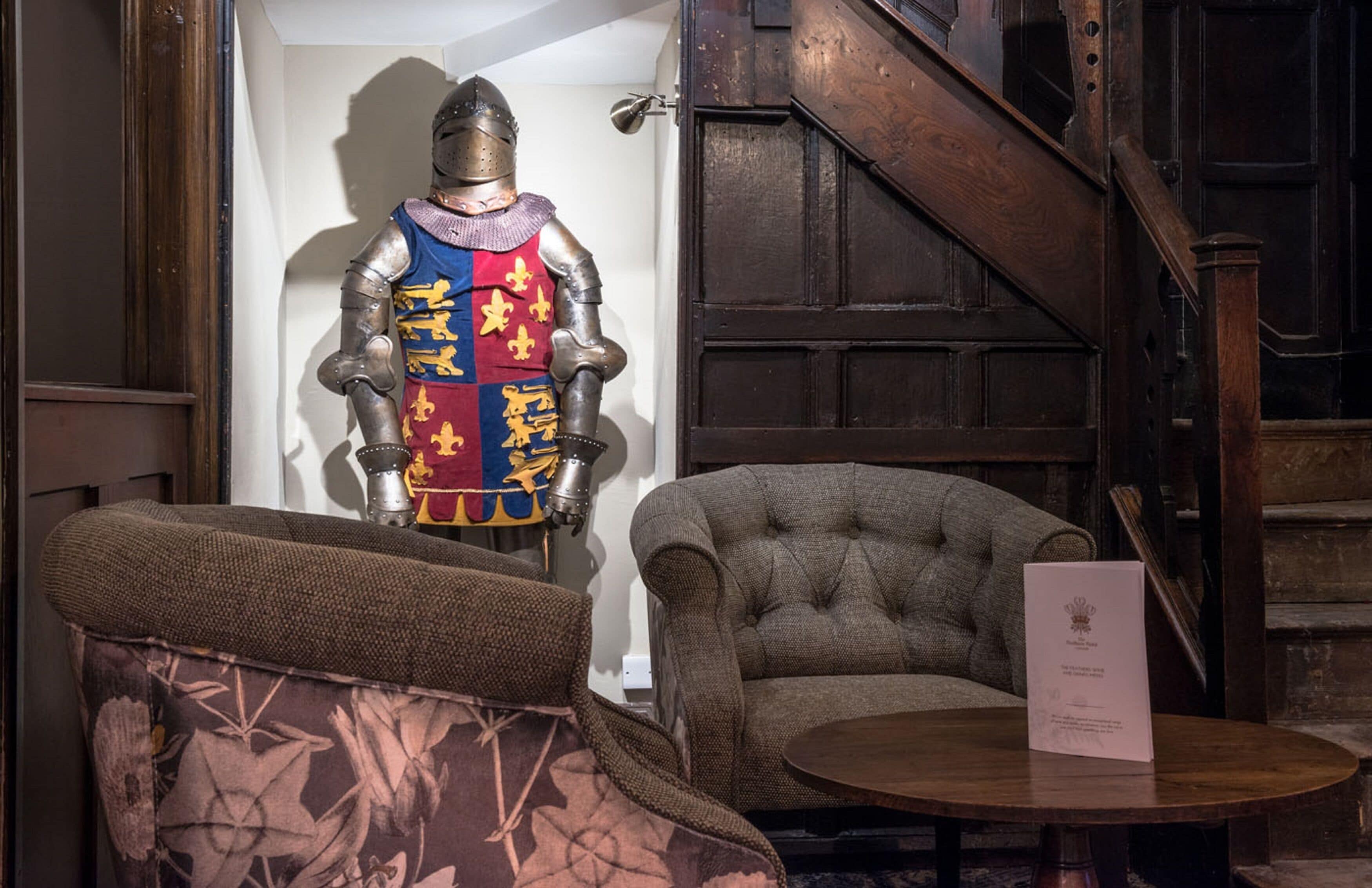 A medieval knight's armor on display, a tufted armchair, and a wooden staircase.
