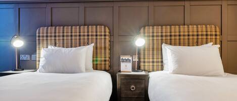 Une chambre d’hôtel avec deux lits, chacun doté d’une tête de lit à carreaux, de linge de lit blanc et de lampes de chevet.