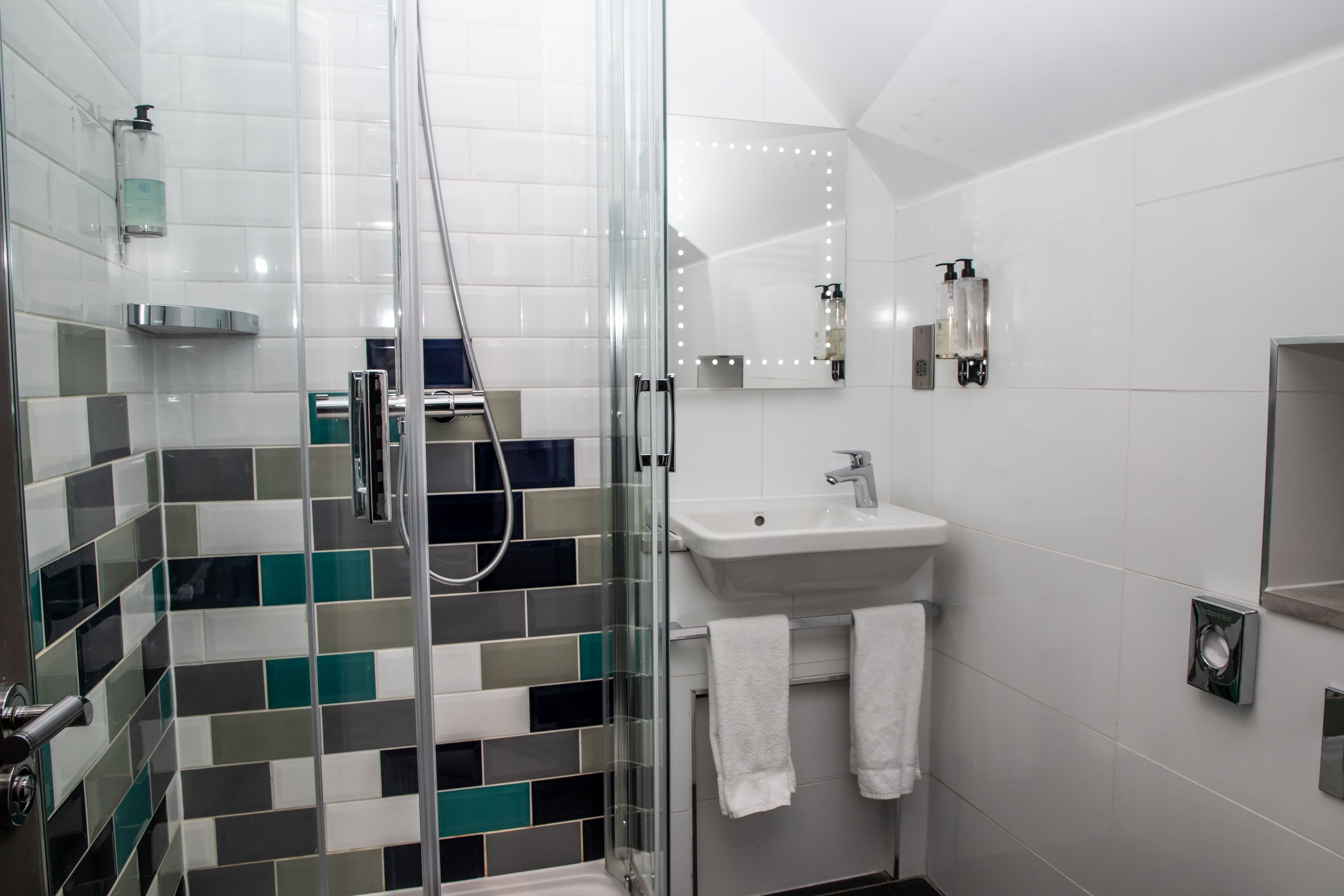 A modern bathroom with a glass shower enclosure, a white sink, and a mirror with lights.