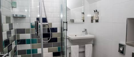 A modern bathroom with a glass shower enclosure, a white sink, and a mirror with lights.
