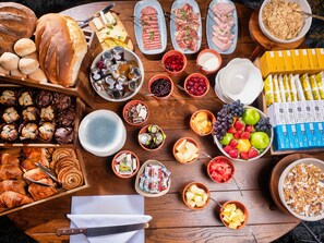 A variety of food items including bread, pastries, cheeses, meats, fruits, and beverages arranged on a wooden table. - The Feathers Hotel (Ludlow)