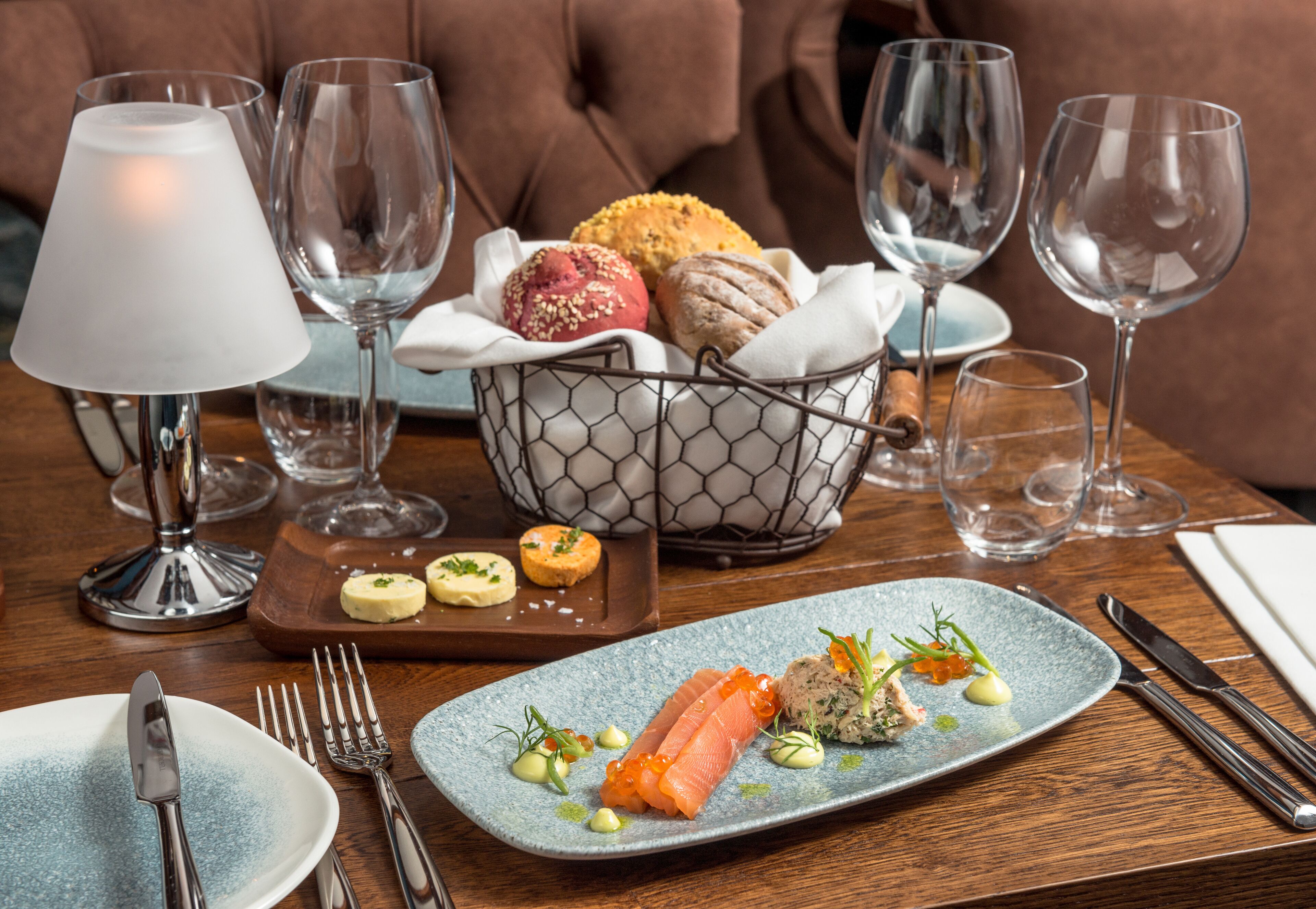 A dining table with a plate of food, cutlery, and a basket of bread.