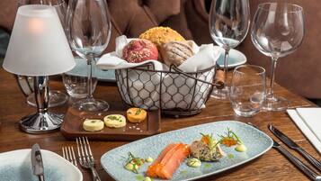 A dining table with a plate of food, cutlery, and a basket of bread.