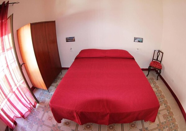 A bedroom with a bed, a chair, a wardrobe, and a door.