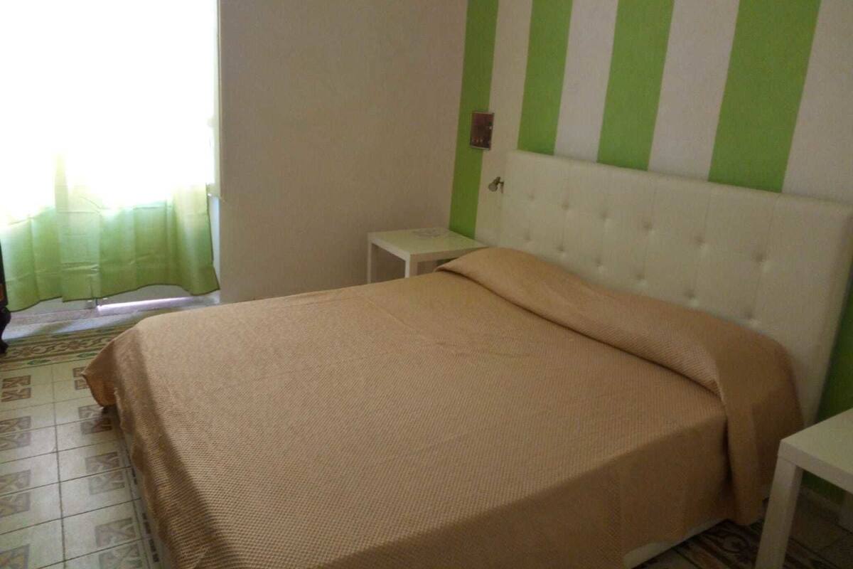 A bedroom with a bed, a nightstand, and a window with curtains.