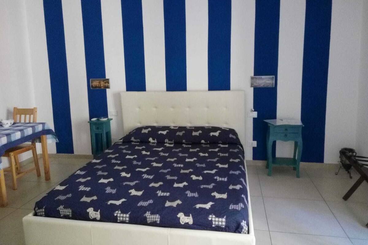 A bedroom with a bed, a chair, a small table, and a nightstand.