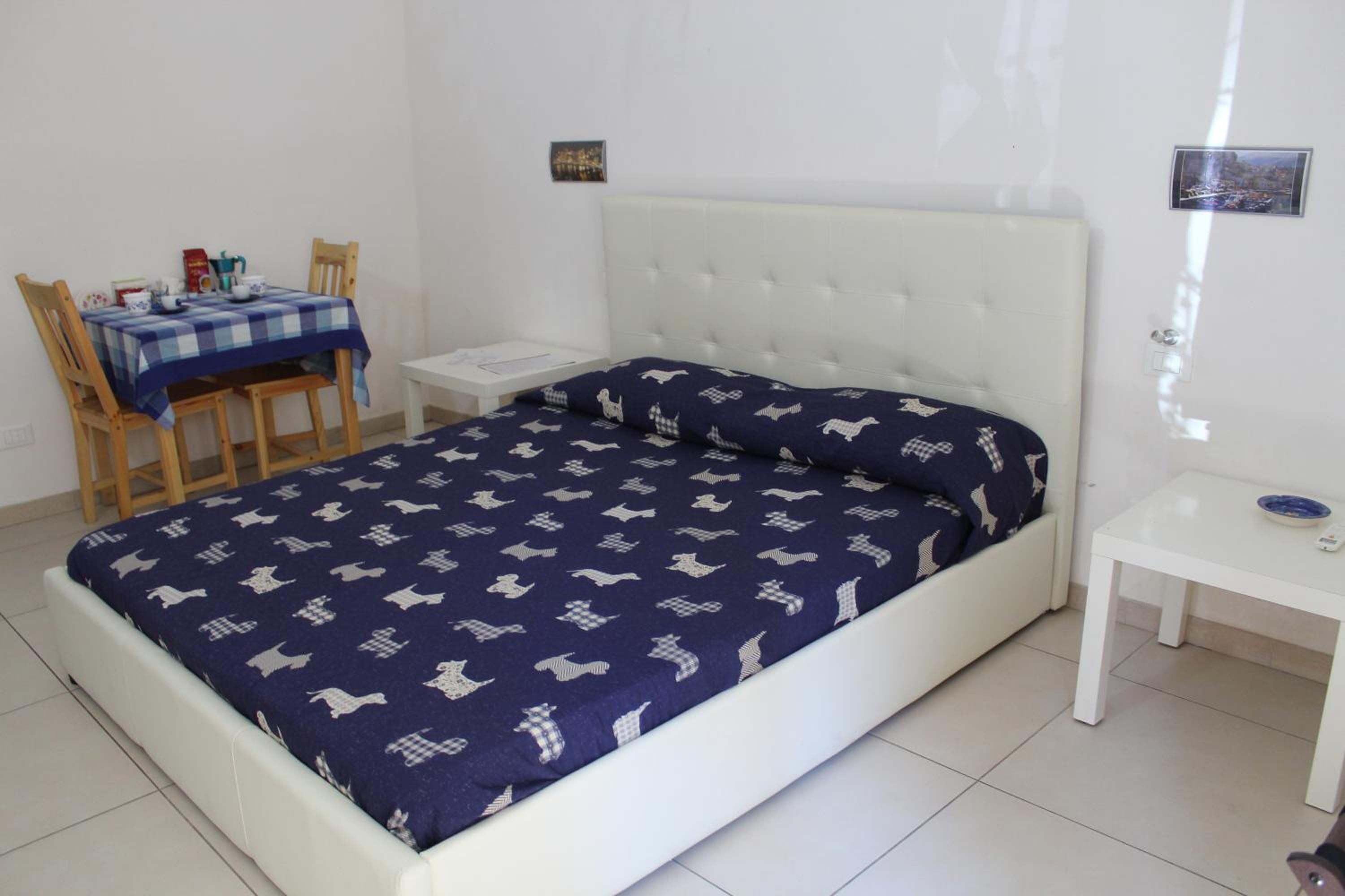 A bedroom with a bed, a table, chairs, and a small white nightstand.