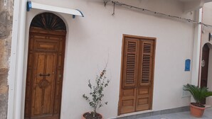 Fachada de edificio con puerta de madera, planta en maceta y ventana con contraventanas.