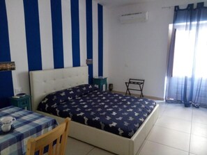 Un dormitorio con una cama, una mesa con mantel a cuadros, una silla y una mesita de noche.
